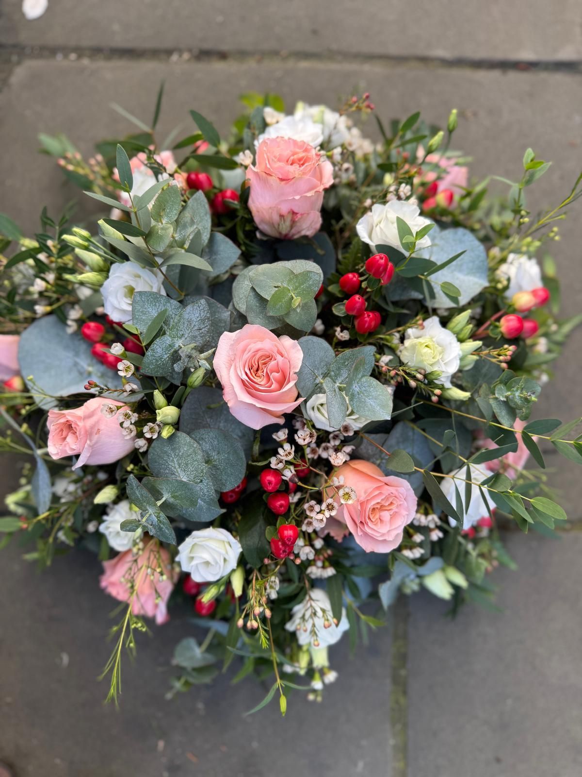 Pink and white roses with berries and eucalyptus in a floral arrangement.