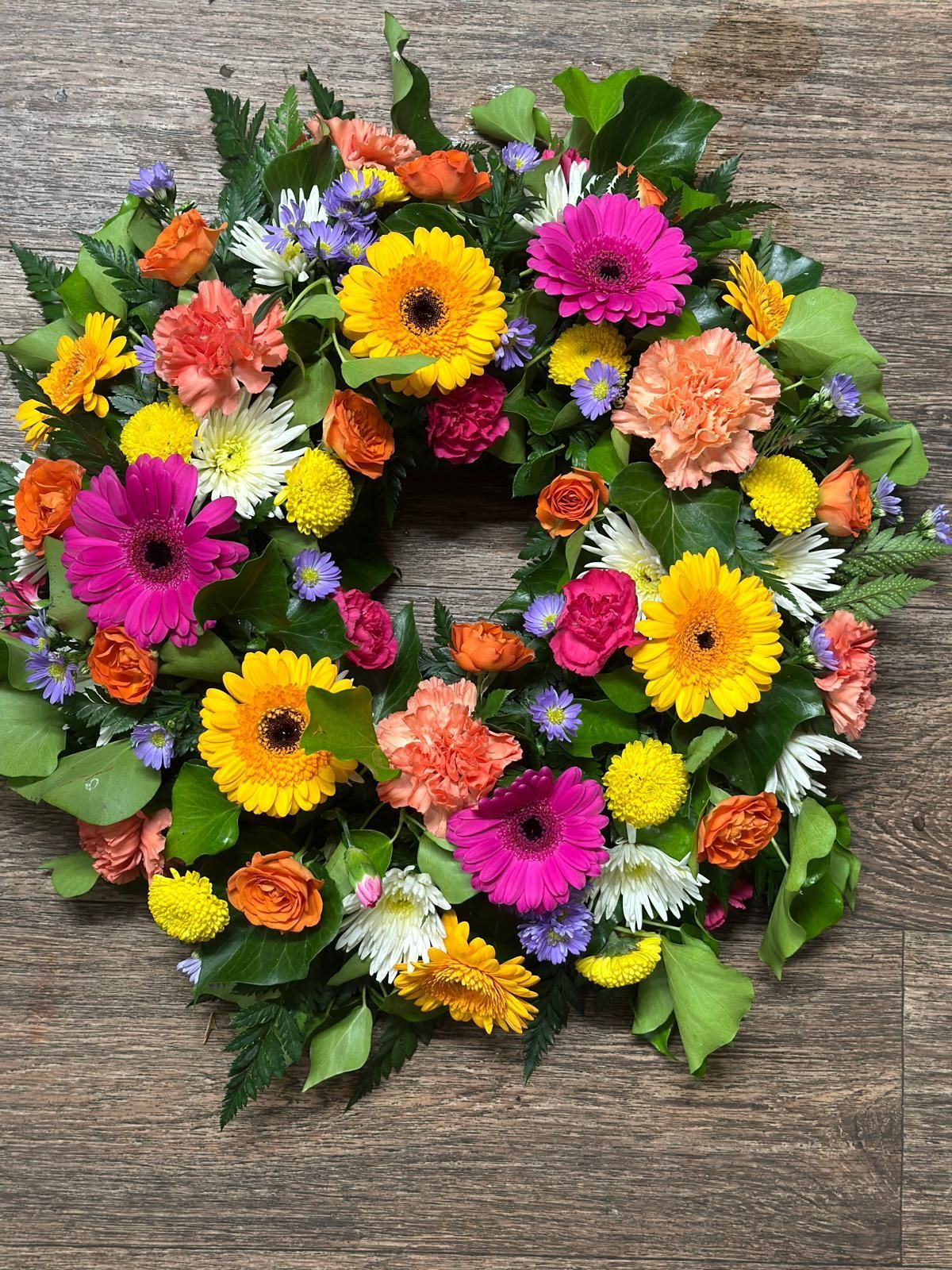 Colorful floral wreath with pink, yellow, orange and white flowers on a wood surface.