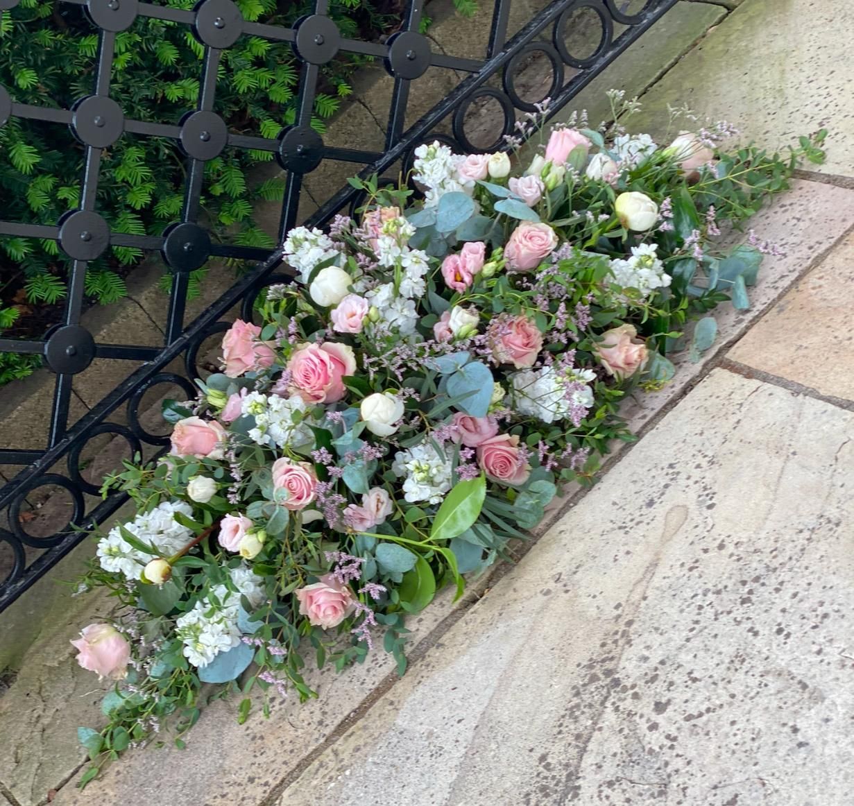 Floral arrangement of pink roses and white flowers, placed on stone steps near a black iron railing.