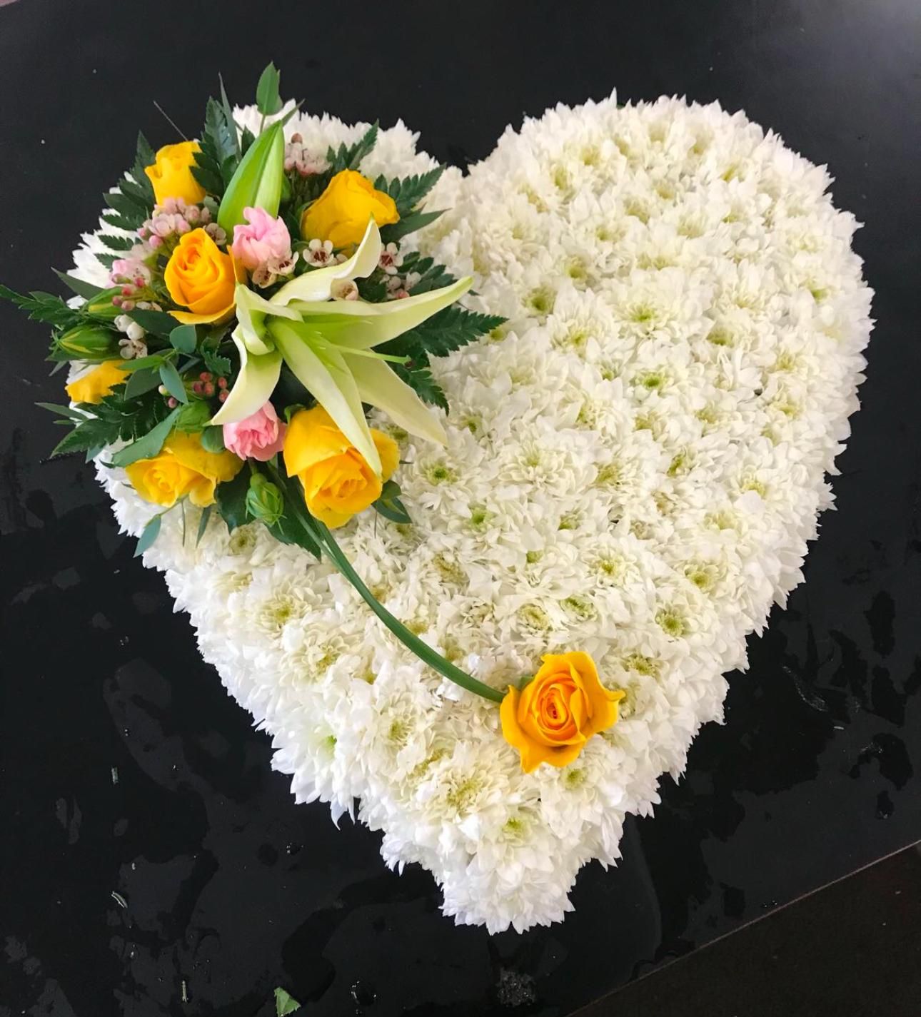 Heart-shaped floral arrangement of white flowers with yellow roses, pink buds, and a lily.