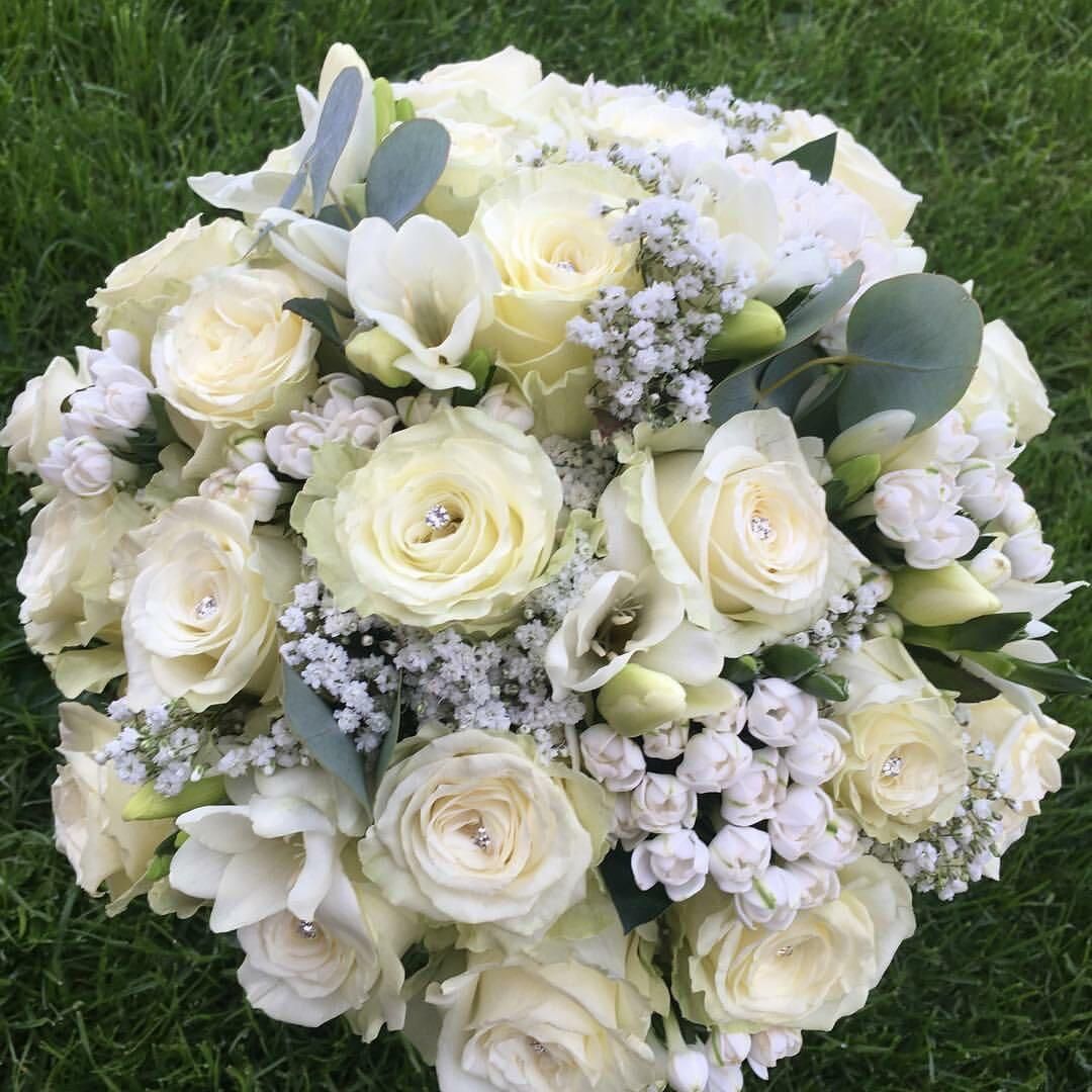 White rose and freesia bridal bouquet with baby's breath and eucalyptus on green grass.