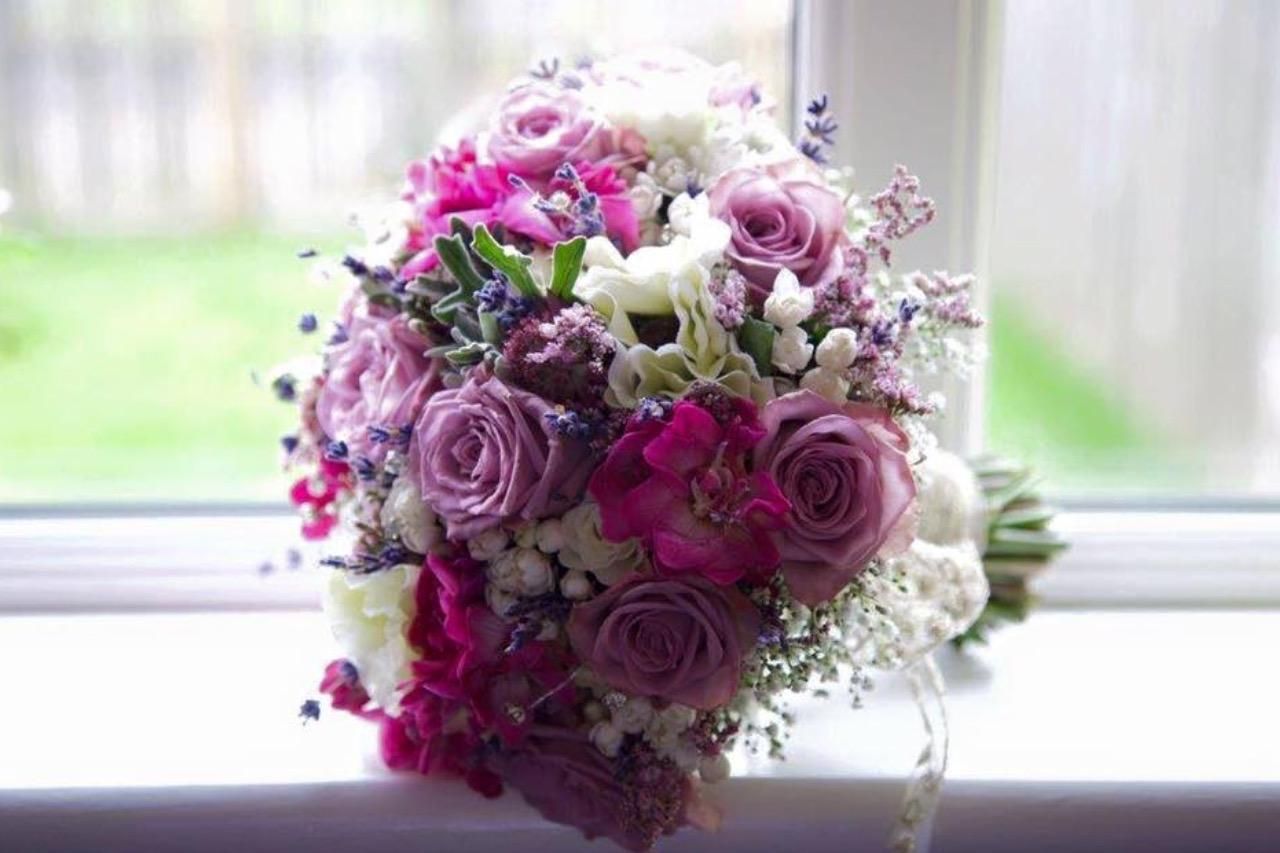 Bouquet of pink and lavender roses and white flowers on a windowsill, with a blurred green background.