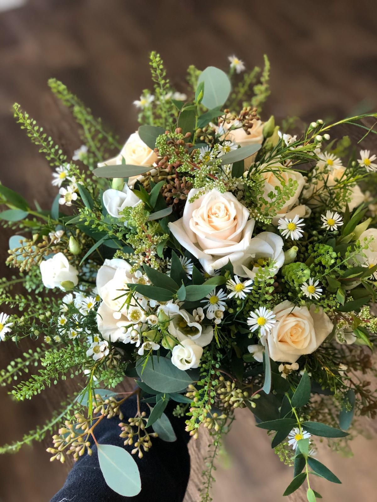 Cream and white rose bouquet with green foliage and daisies.