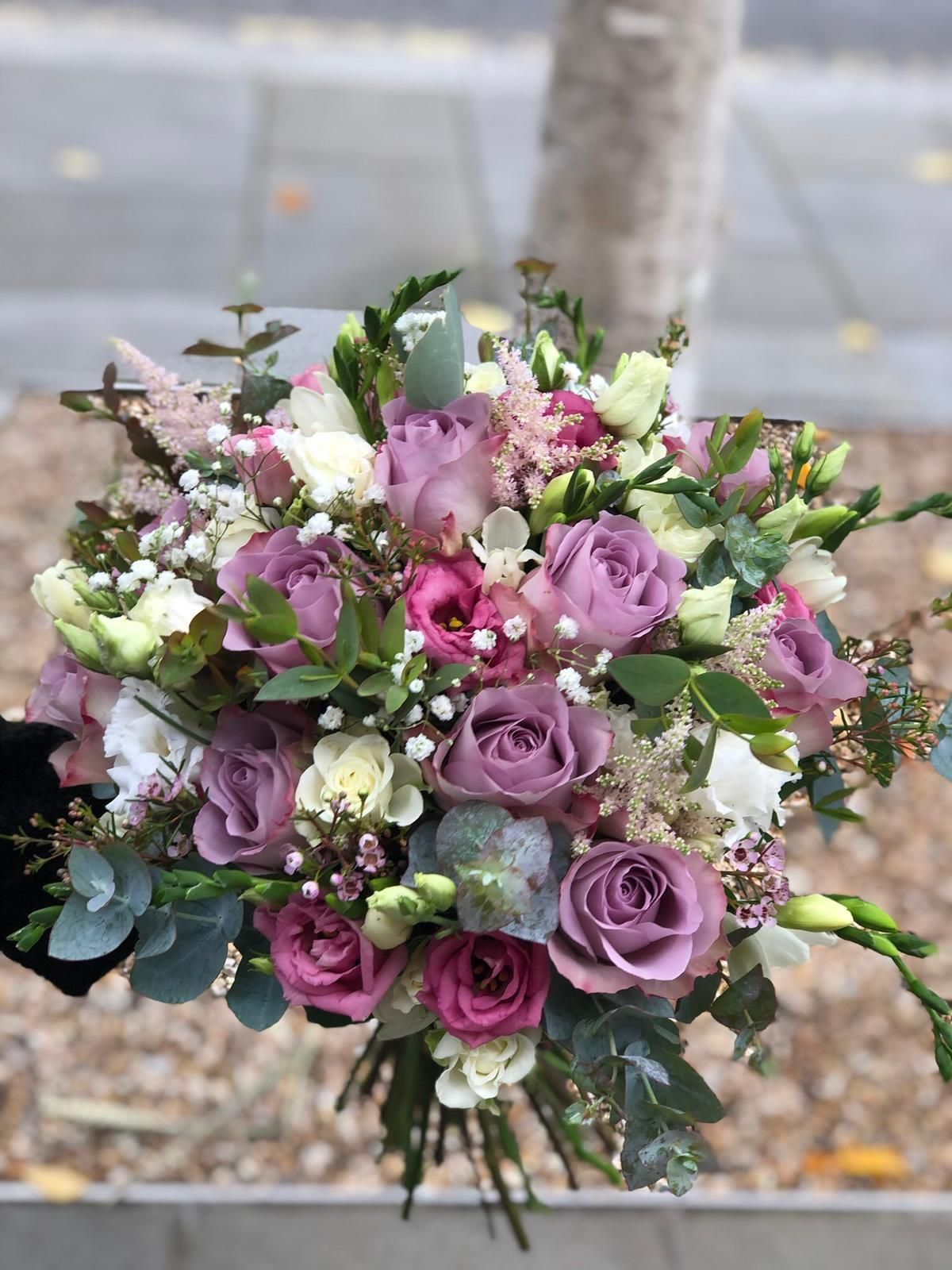 Bouquet of purple and white flowers with greenery, held against a blurred background.