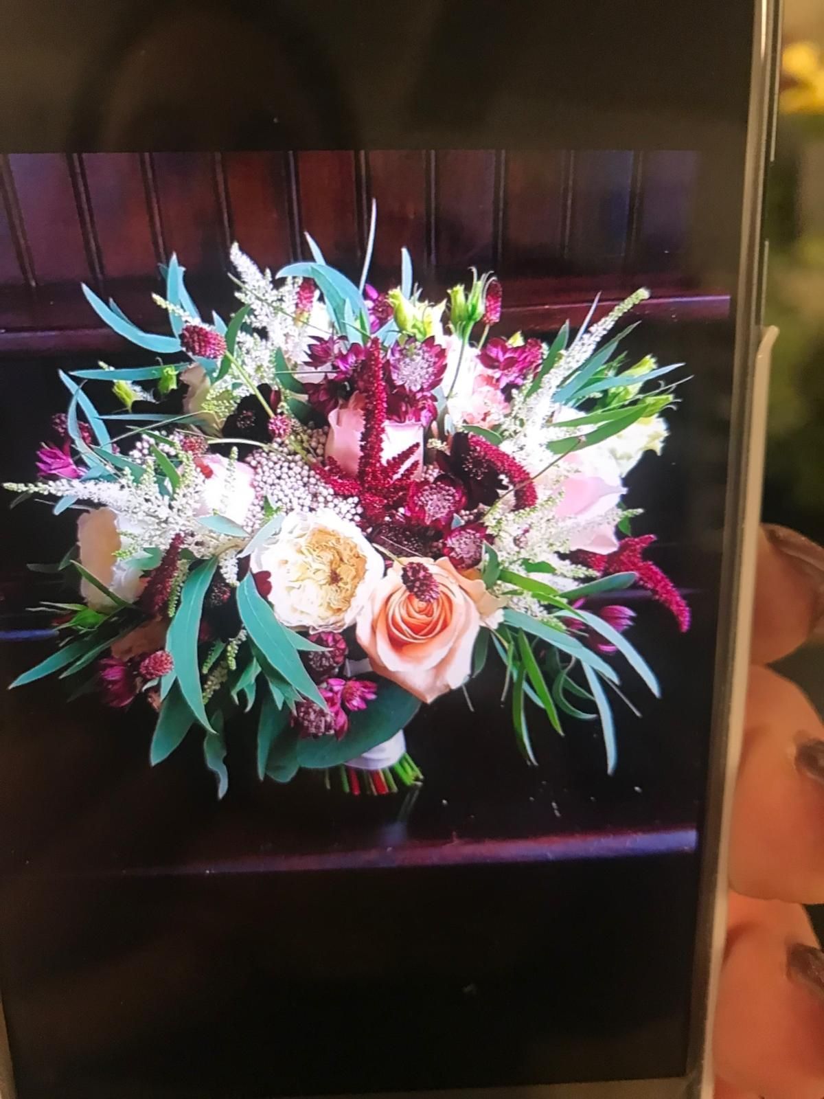 A colorful bouquet with peach roses, deep red flowers, and green foliage on a dark wood surface.