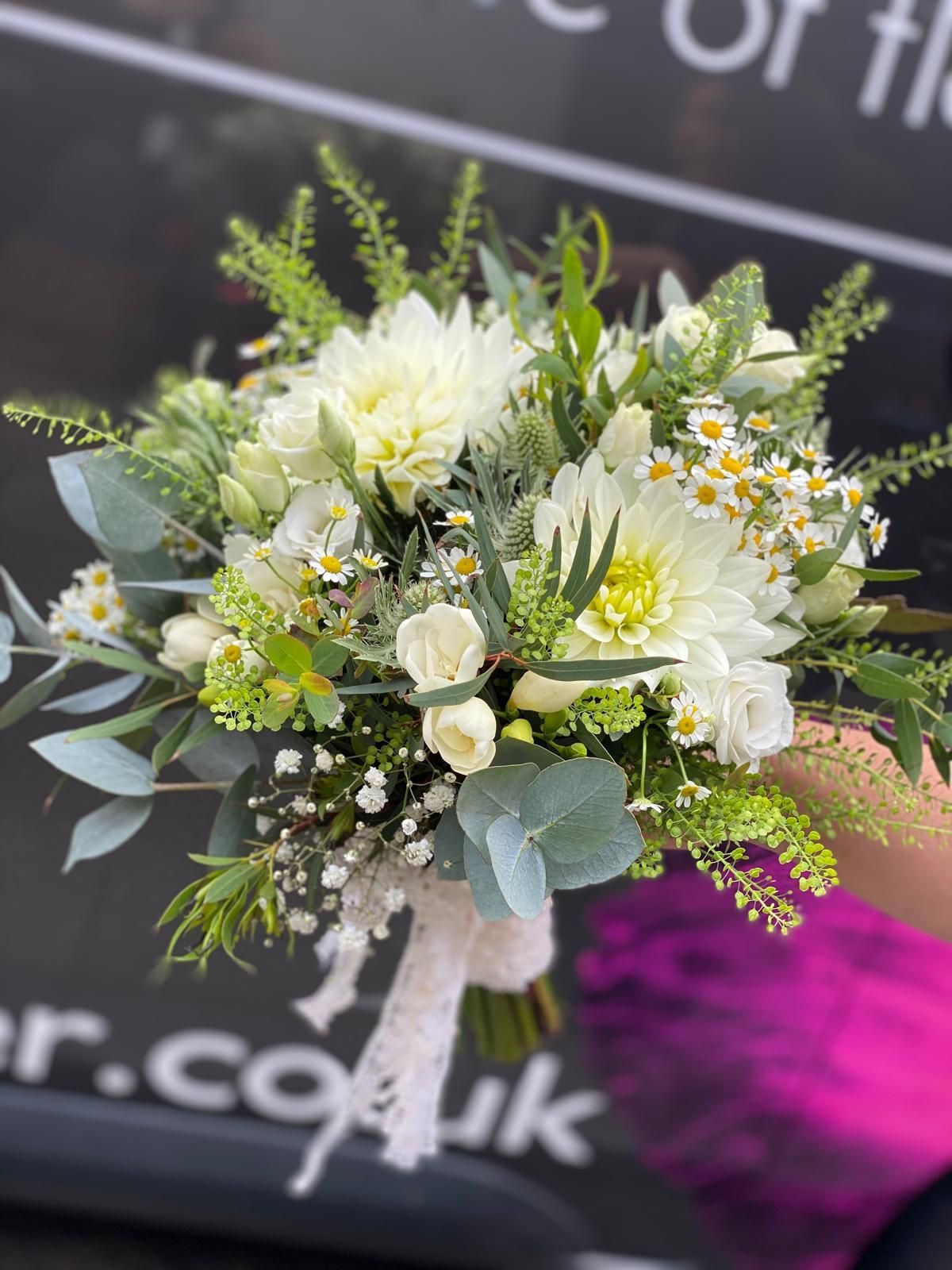 Bouquet of white dahlias, daisies, and greenery tied with lace ribbon.