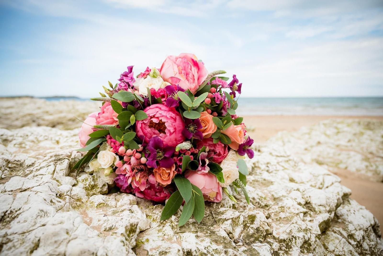 Colorful wedding bouquet on a white rocky surface, with the ocean and sky in the background.