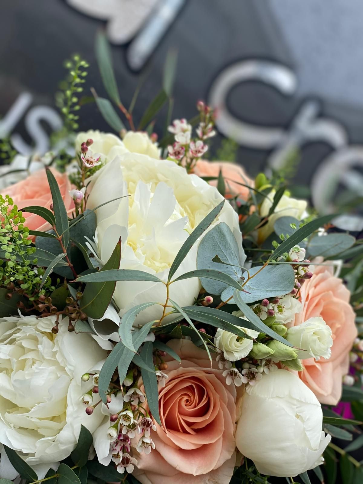 Close-up of a bouquet with white peonies, peach roses, and green eucalyptus leaves.