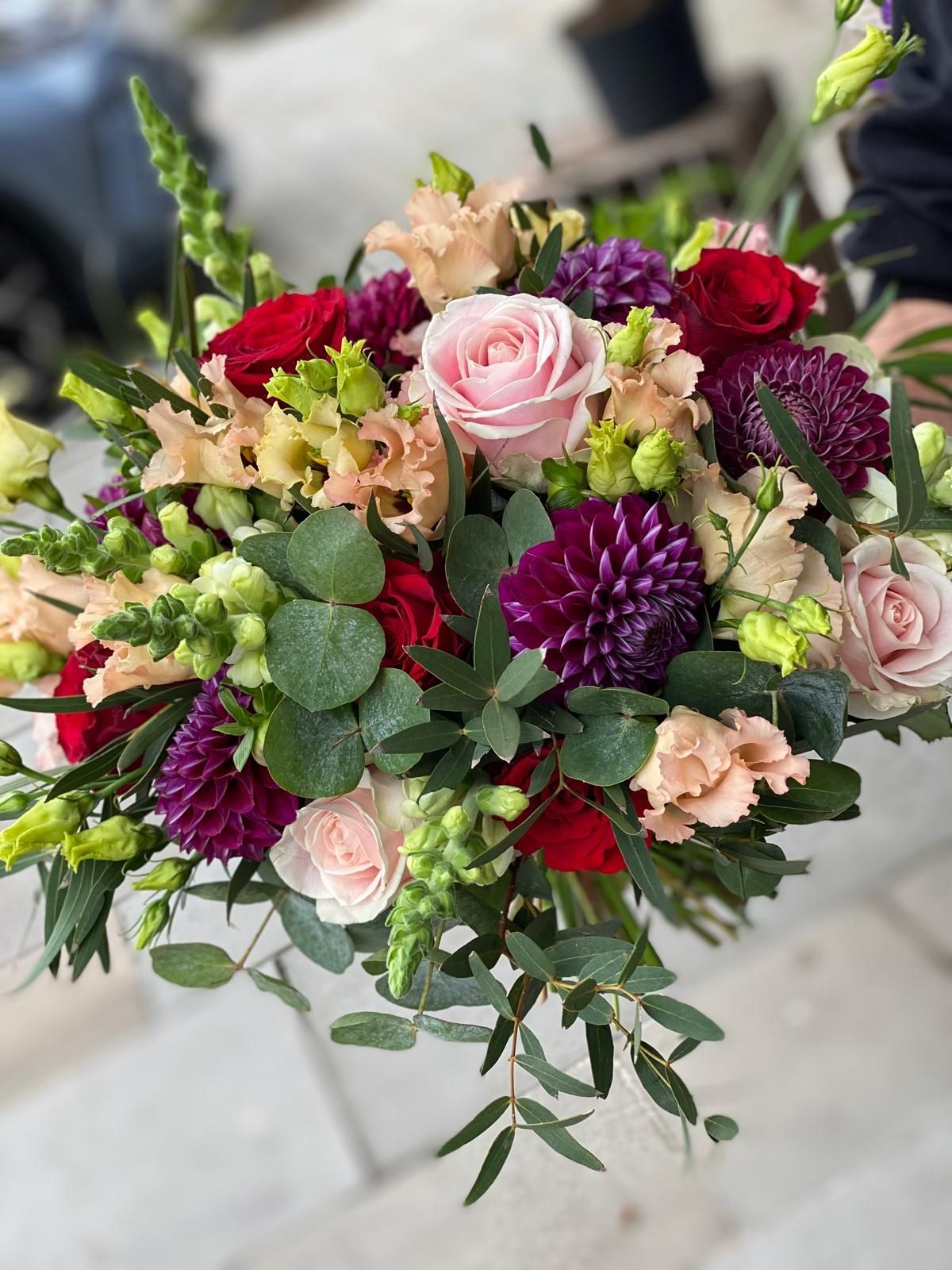 Bouquet of red, pink, and purple flowers with green foliage against a blurred background.