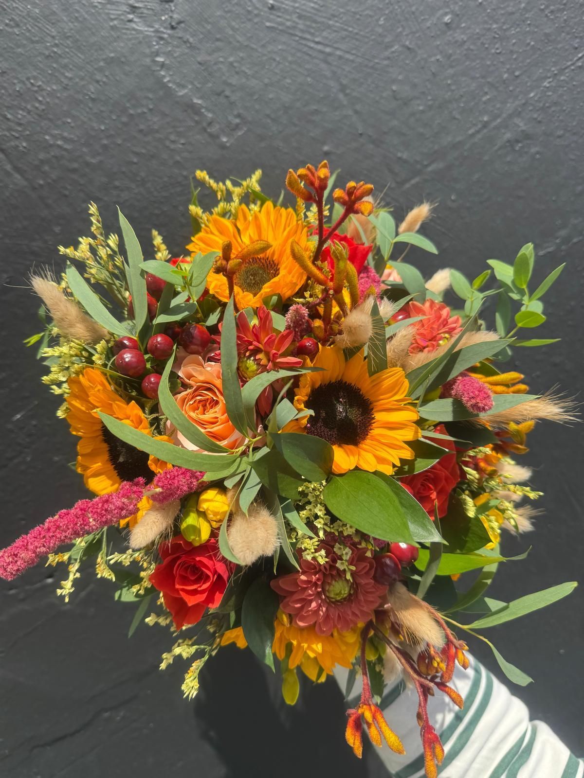 Bouquet of sunflowers, red berries, and orange roses against a dark background.