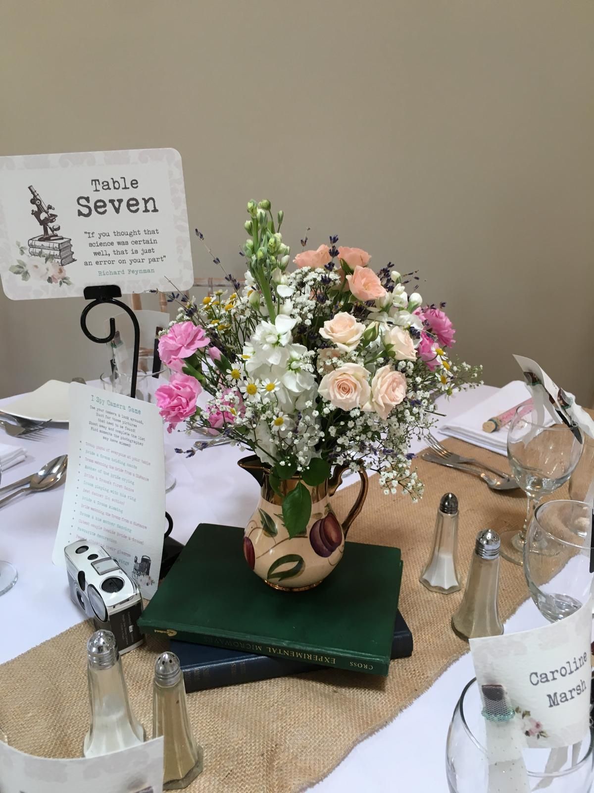 Table setting with flowers in a jug, books, and table number 