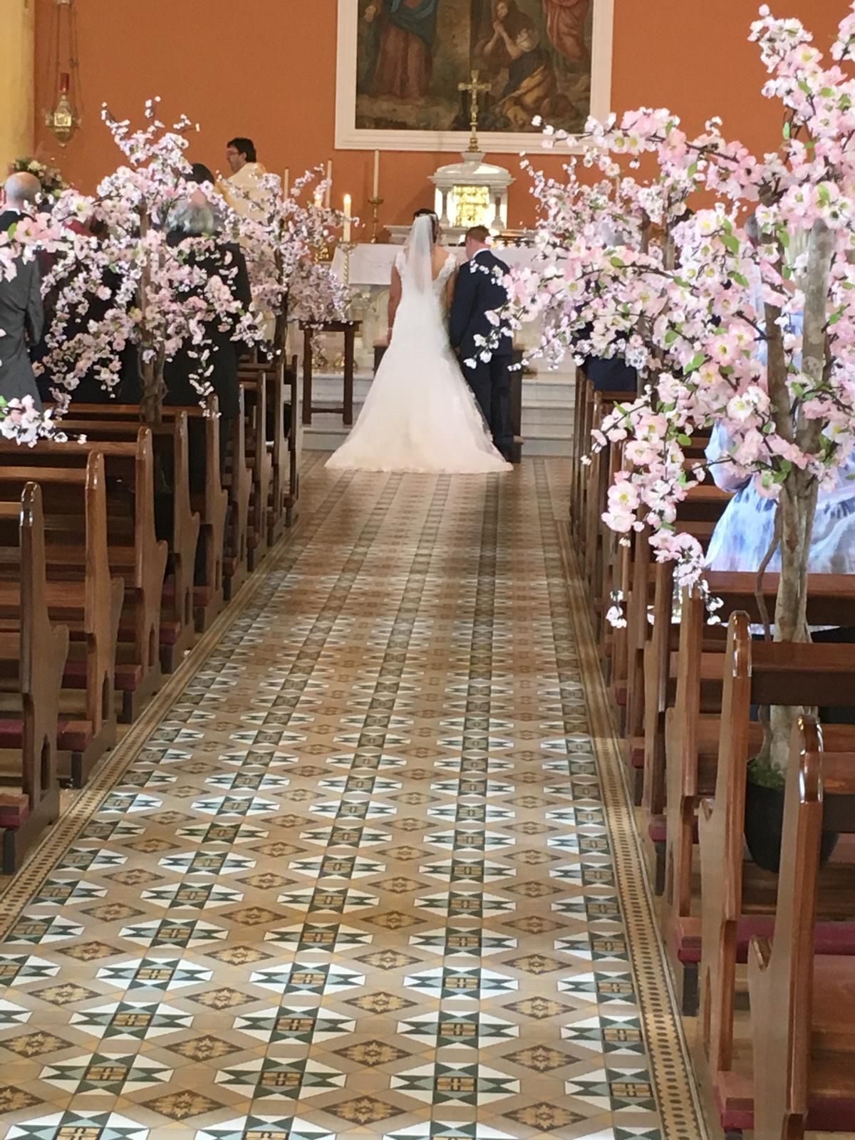 Bride and groom walk down aisle decorated with pink cherry blossom trees in a church.