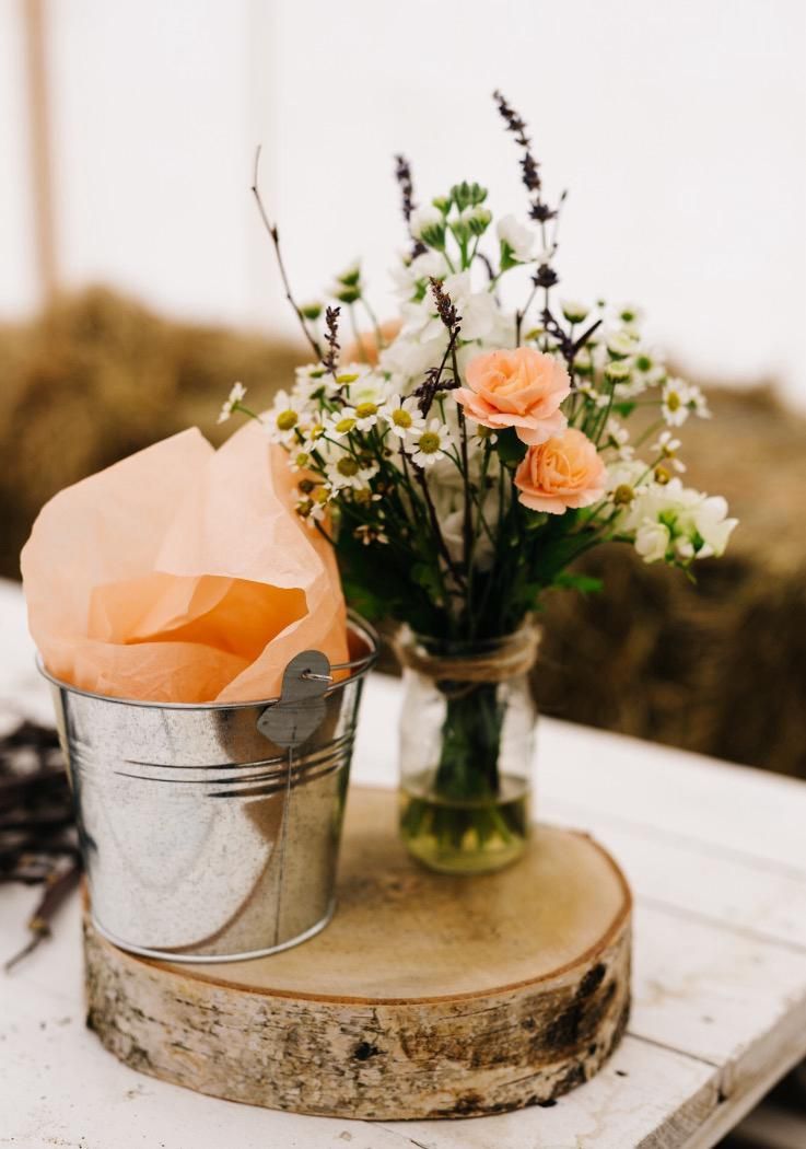 Flowers and favors in a rustic setting: flowers in a jar and gifts in a tin bucket on a wood slice.