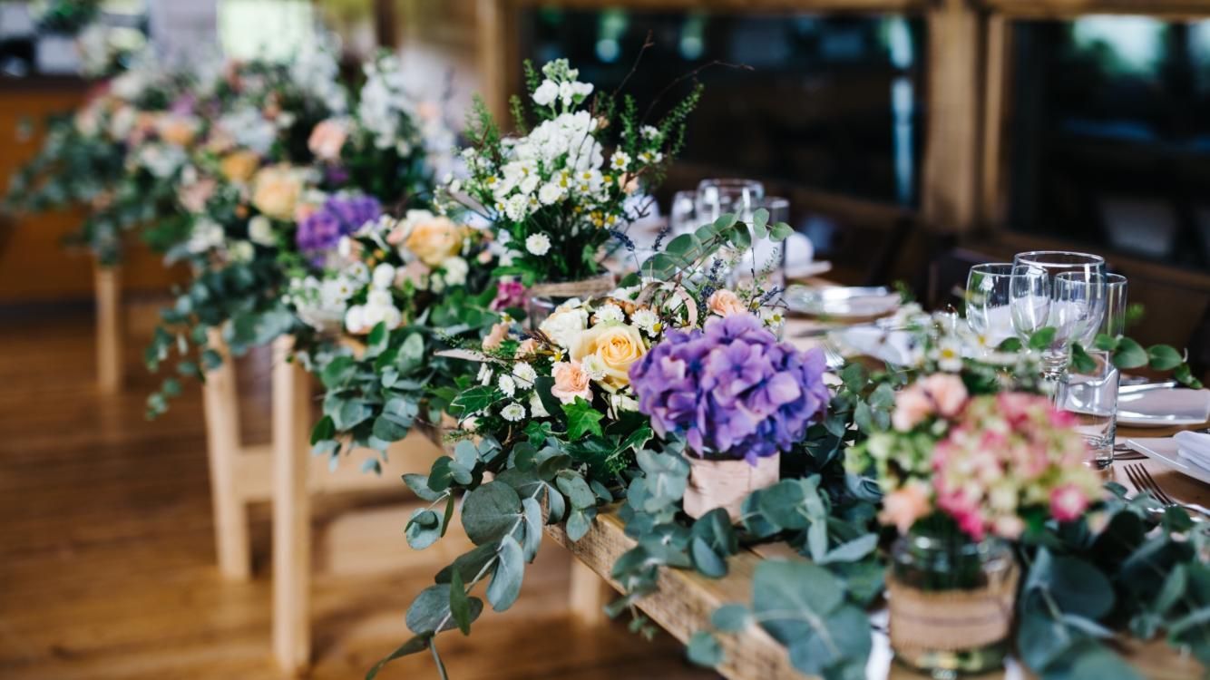 Long wooden table decorated with colorful flowers and greenery for a celebration.
