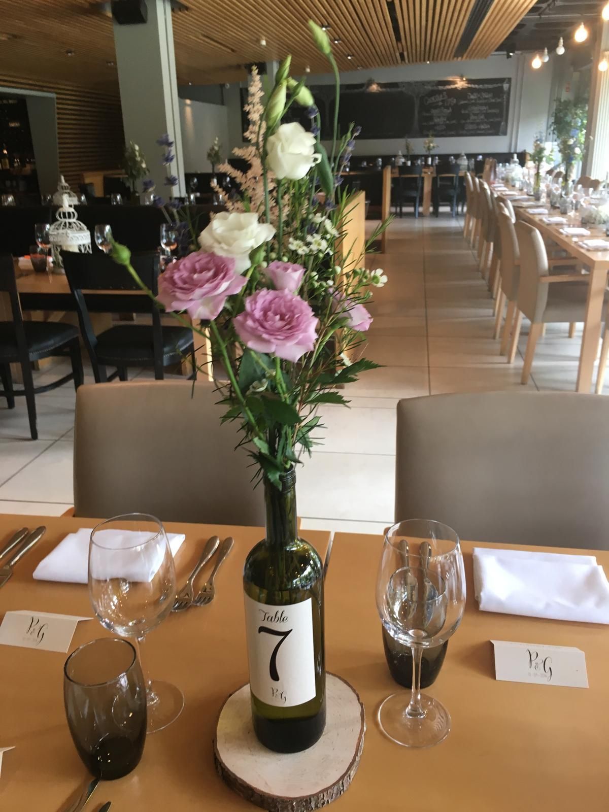Table setting with a floral arrangement in a wine bottle; restaurant interior.