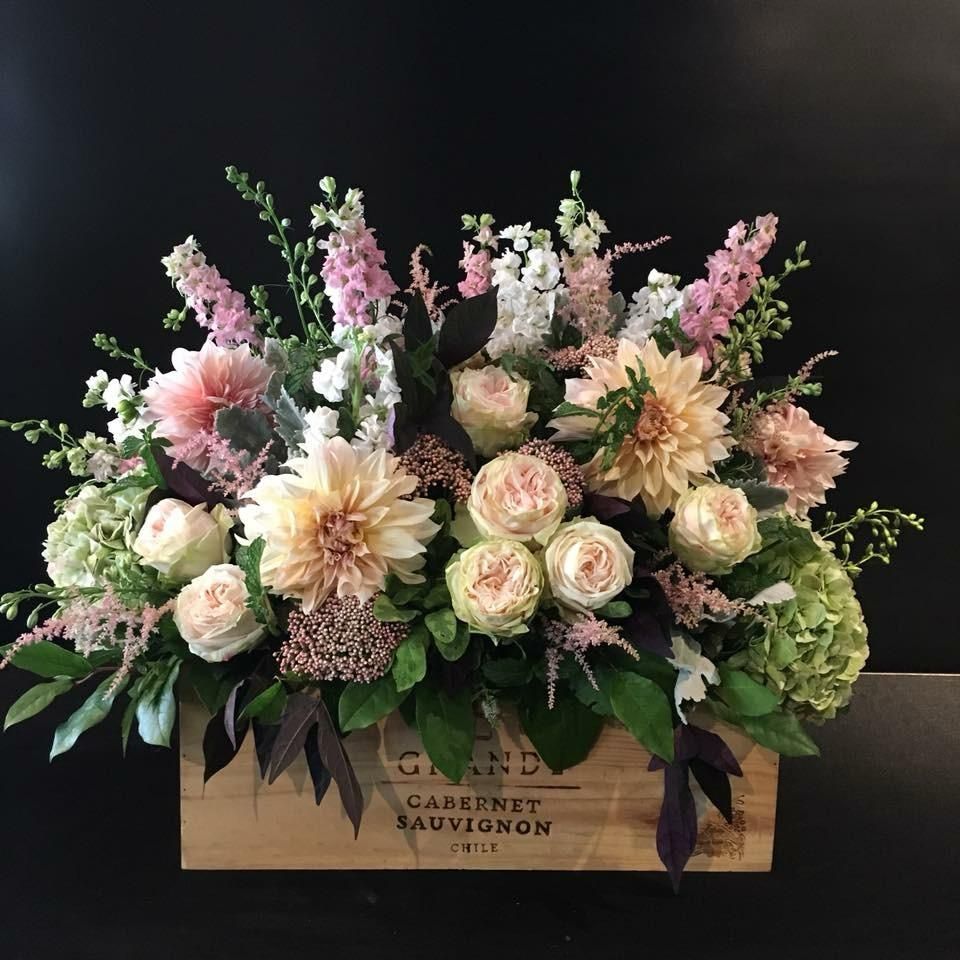 Floral arrangement in a wooden box with pink, peach, and green flowers, against a black backdrop.