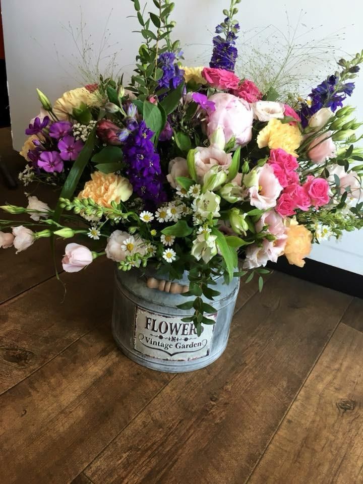 Colorful flower arrangement in a rustic metal bucket, on a wooden floor.