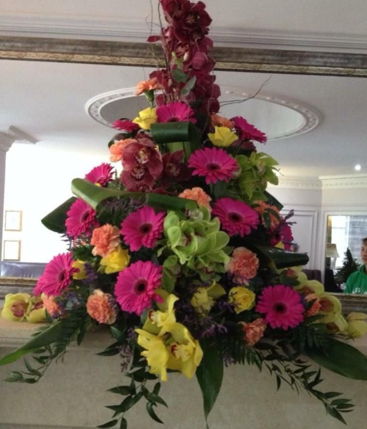 Floral arrangement with pink, yellow, and orange flowers, displayed on a mantle in front of a mirror.