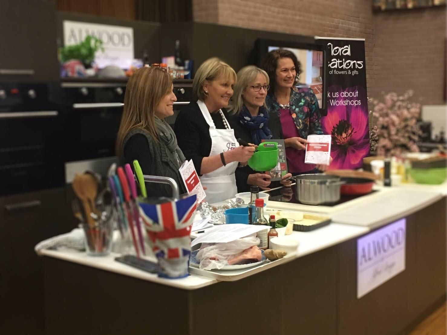 Four women at a cooking demonstration, using kitchen equipment. 