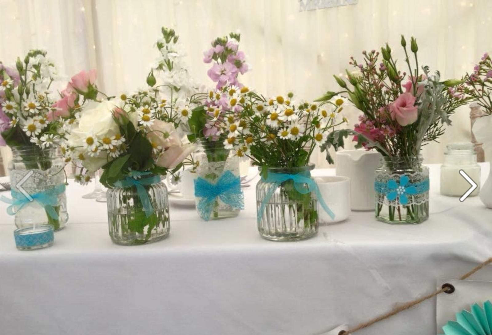 Glass jars with colorful flowers and turquoise ribbons on a white tablecloth.