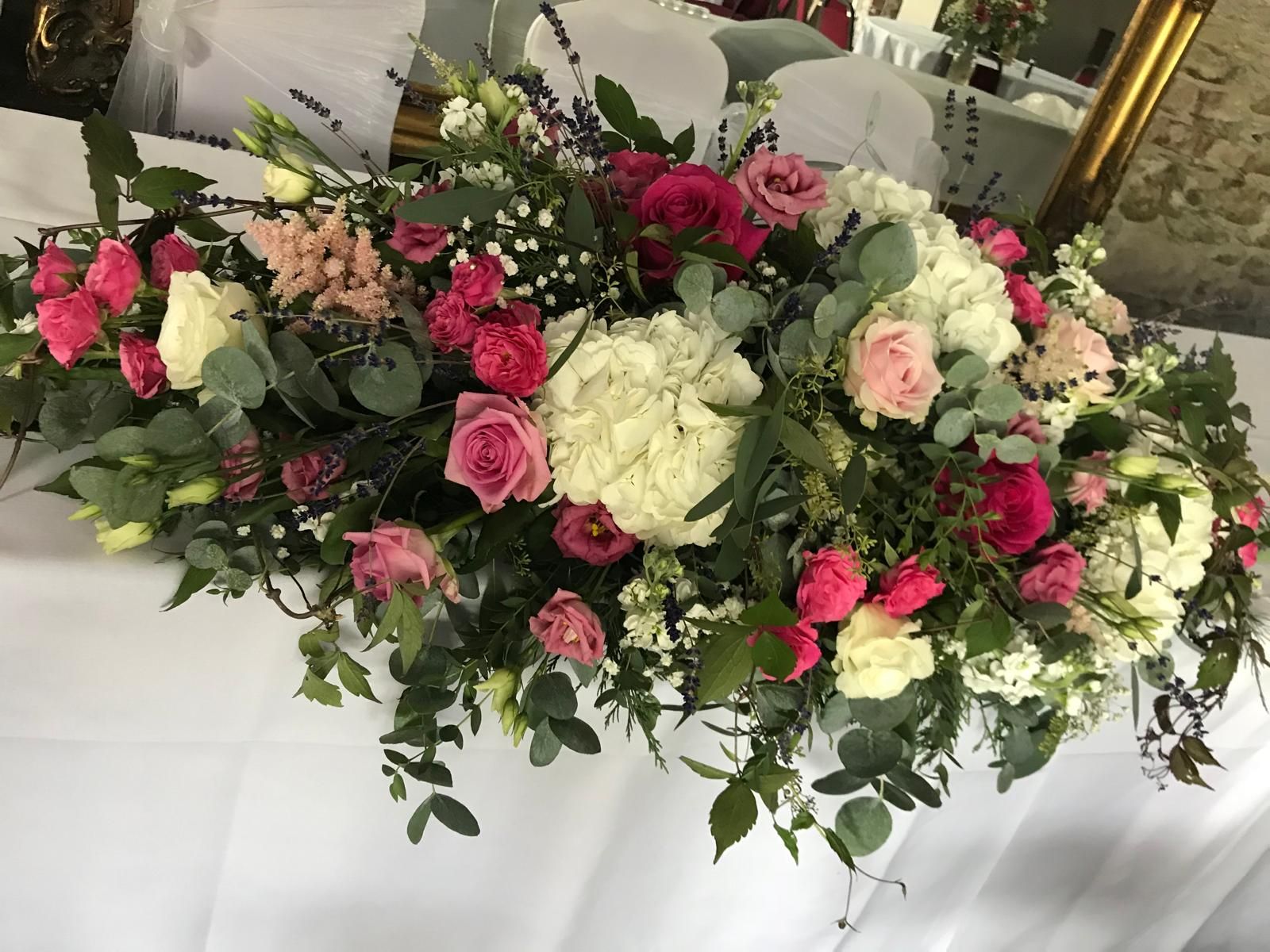 Floral arrangement of pink, white, and green flowers on a white tablecloth.