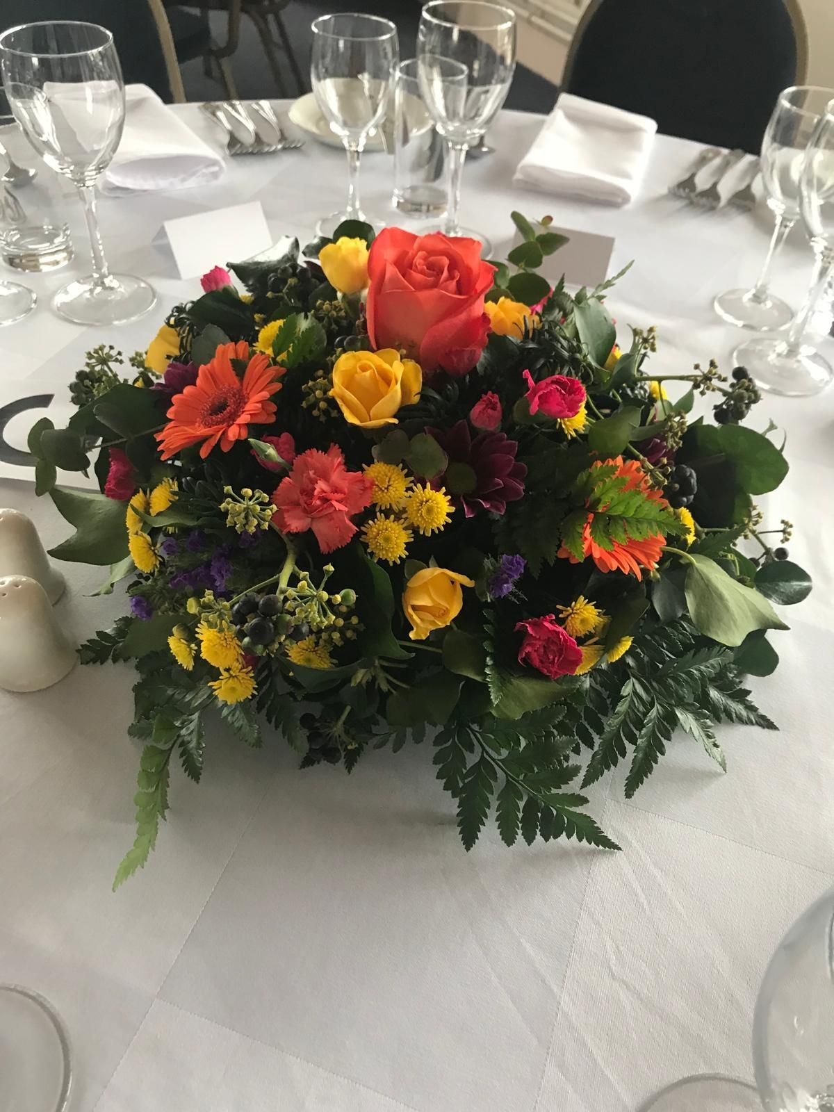 Floral centerpiece on a white tablecloth; orange, yellow, and red flowers with green foliage.