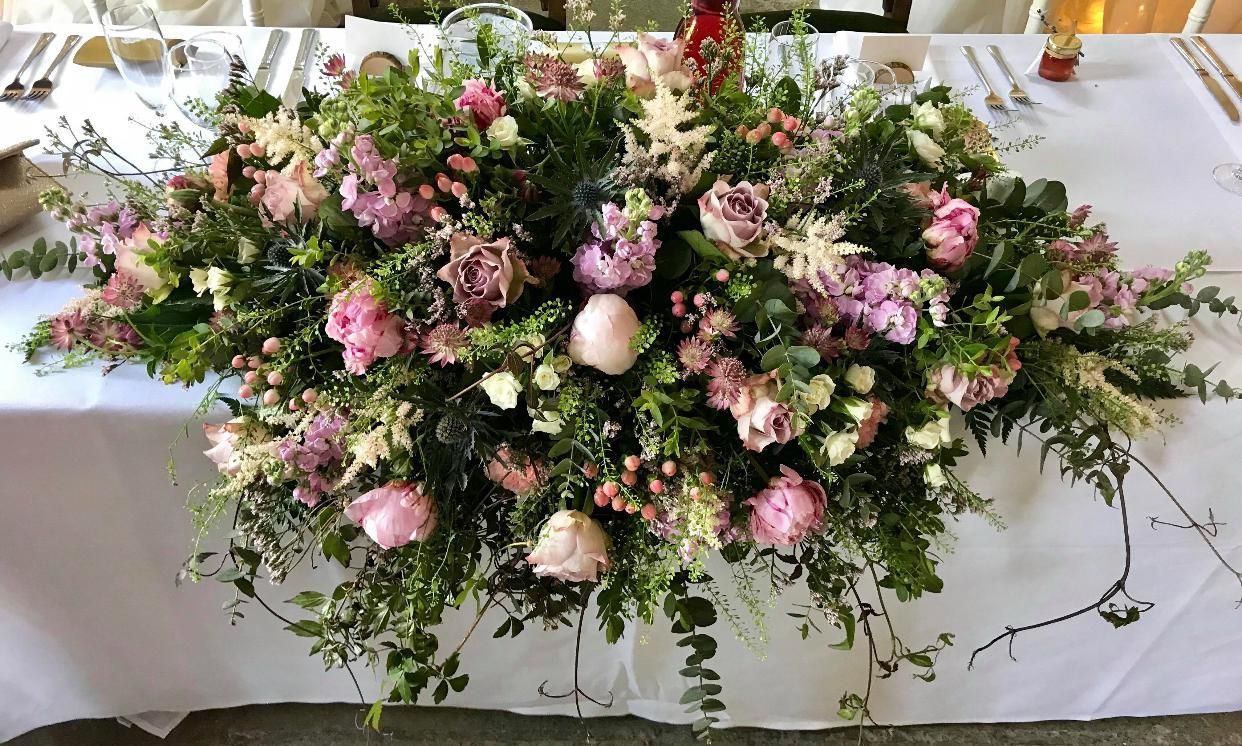 Floral centerpiece on a white tablecloth, featuring pink and purple flowers with greenery.