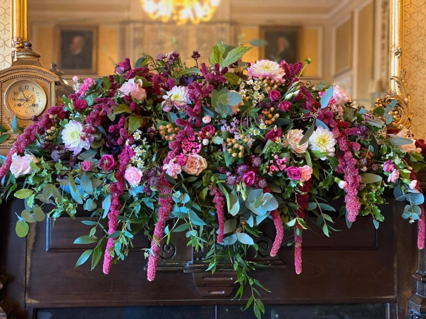 Floral arrangement on a wooden mantle. Flowers are pink, red, and white with green foliage.