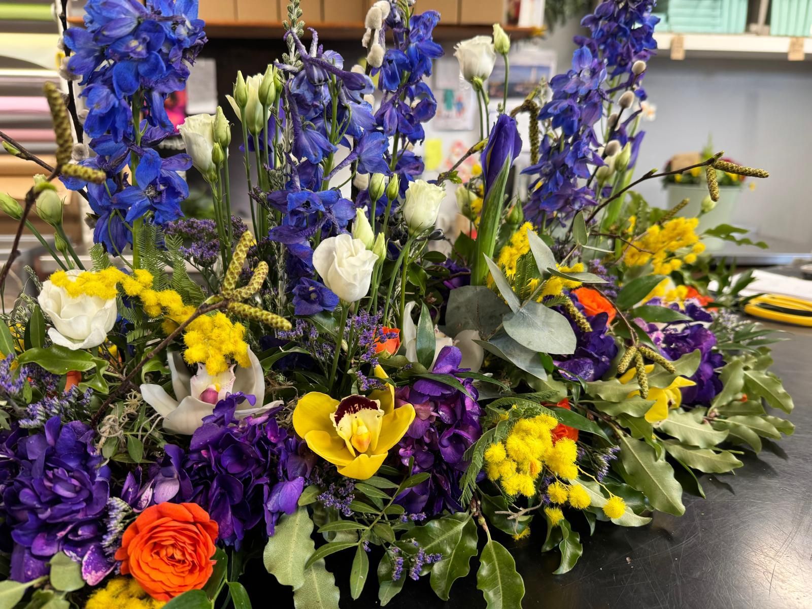 Floral arrangement with blue, purple, yellow, and orange flowers on a table.