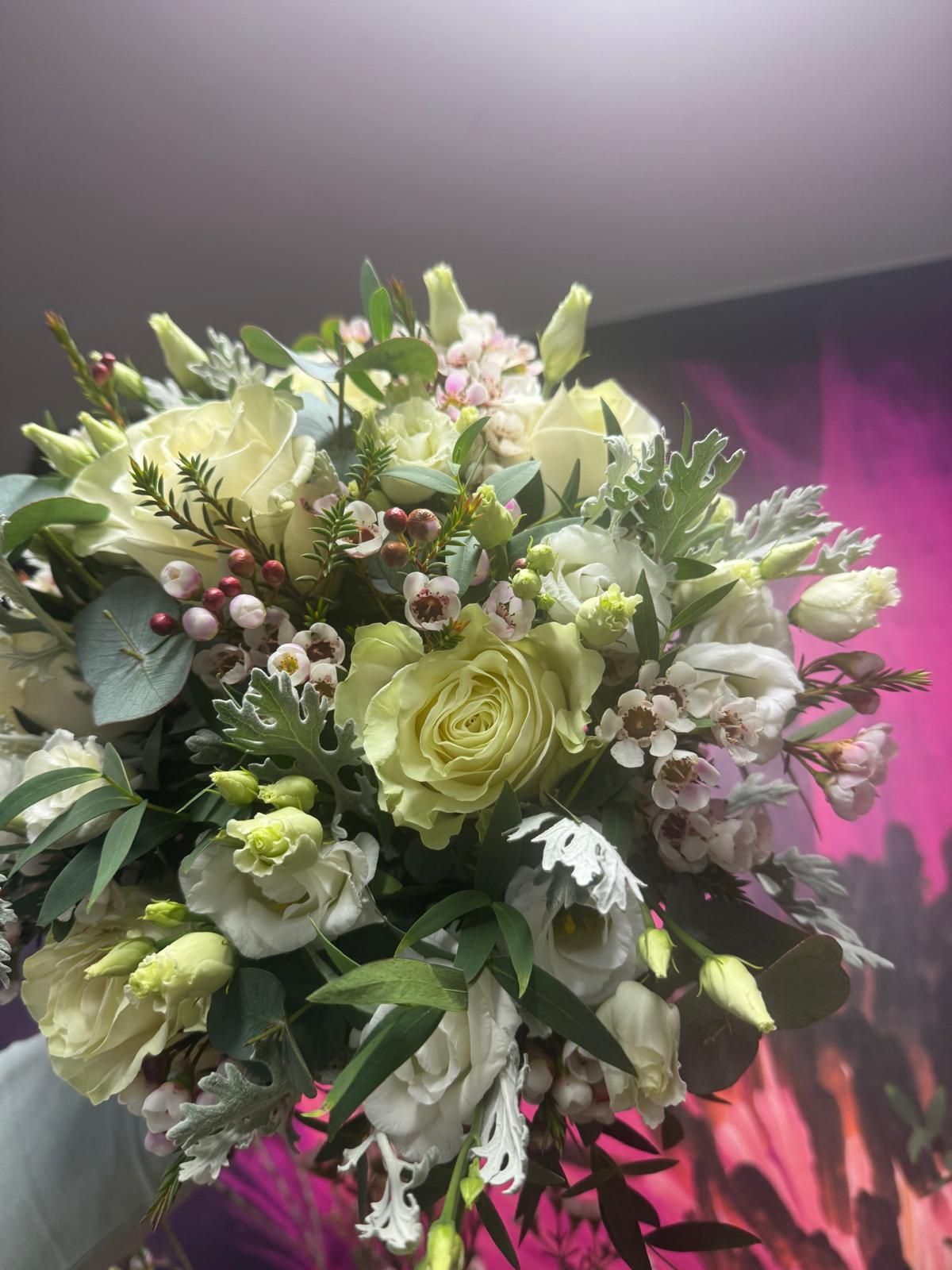 A bouquet of pale yellow and white flowers with greenery, held in hand.
