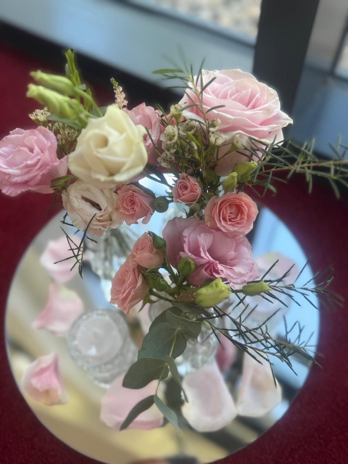 Floral arrangement of pink and white roses on a mirrored surface, with scattered petals.