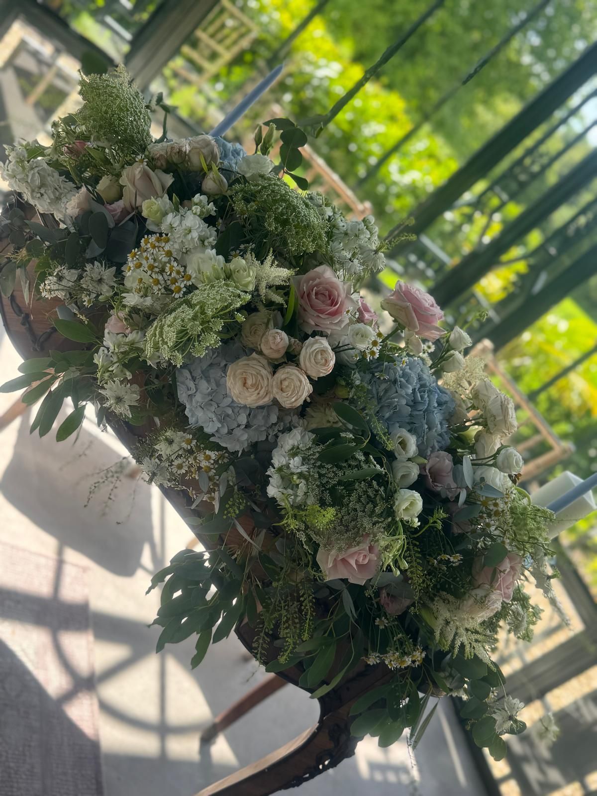 Floral arrangement on a moss-covered log with hydrangeas, roses, and greenery, against a blurred bamboo backdrop.