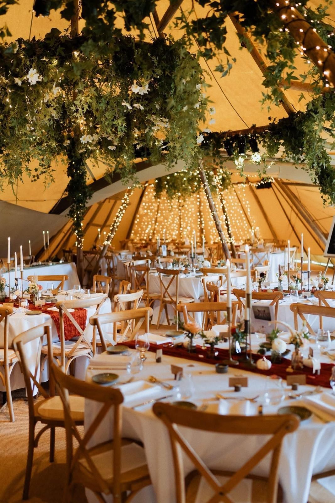 Wedding reception in a tent, decorated with string lights, greenery, and candles. Tables set with white linens.