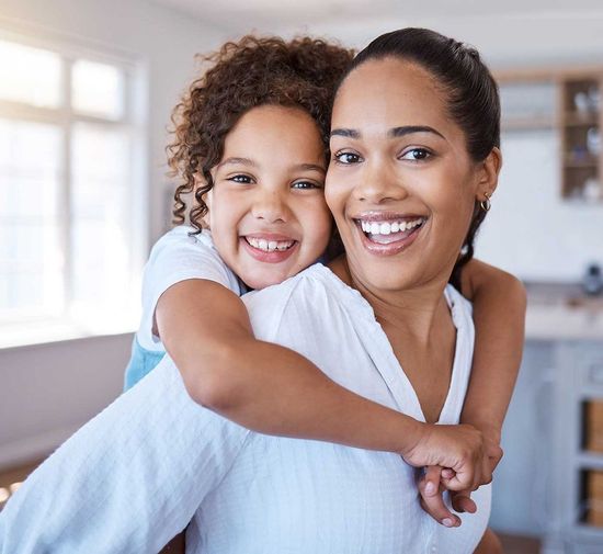 A woman is giving a little girl a piggyback ride.