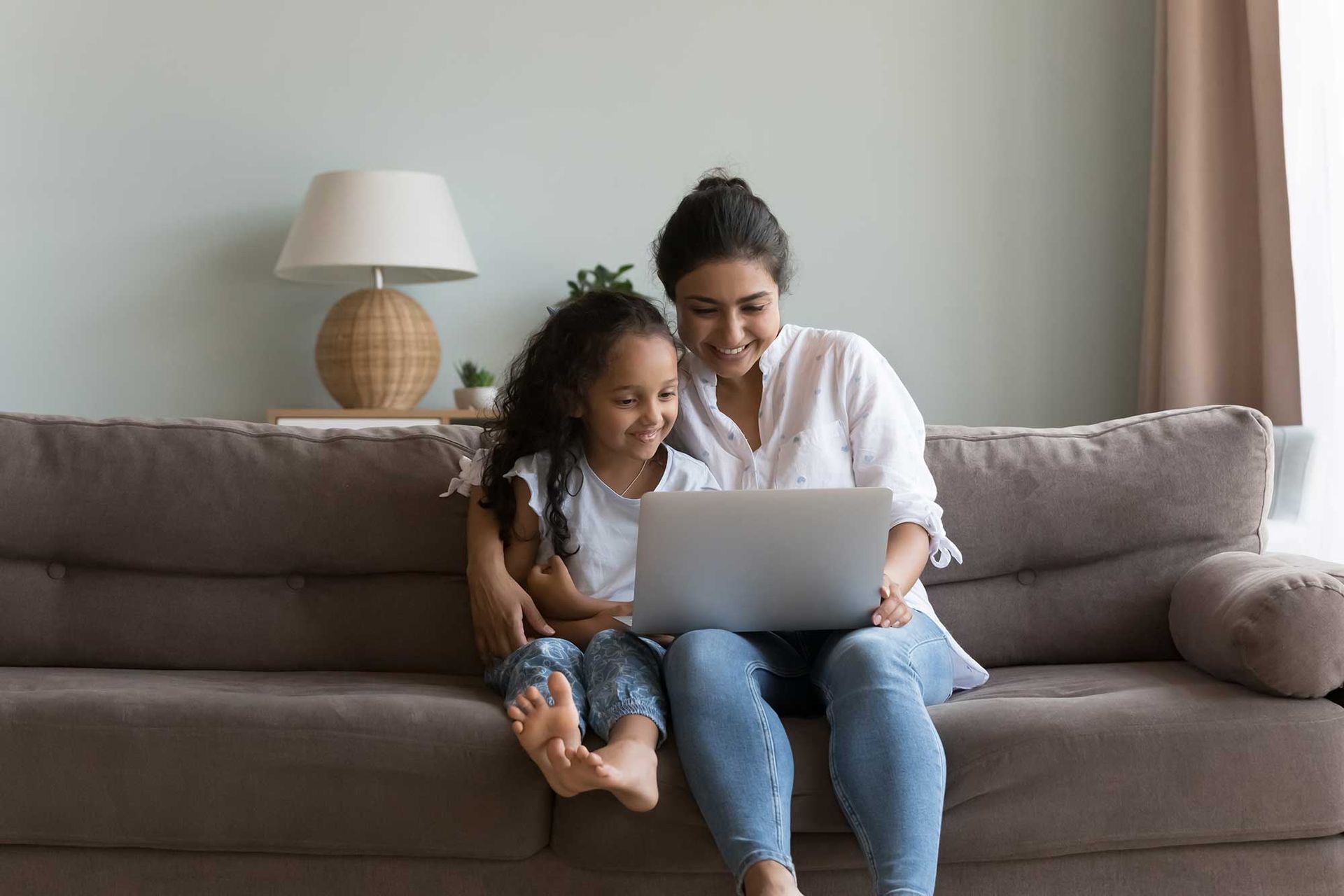 A woman and a little girl are sitting on a couch looking at a laptop.