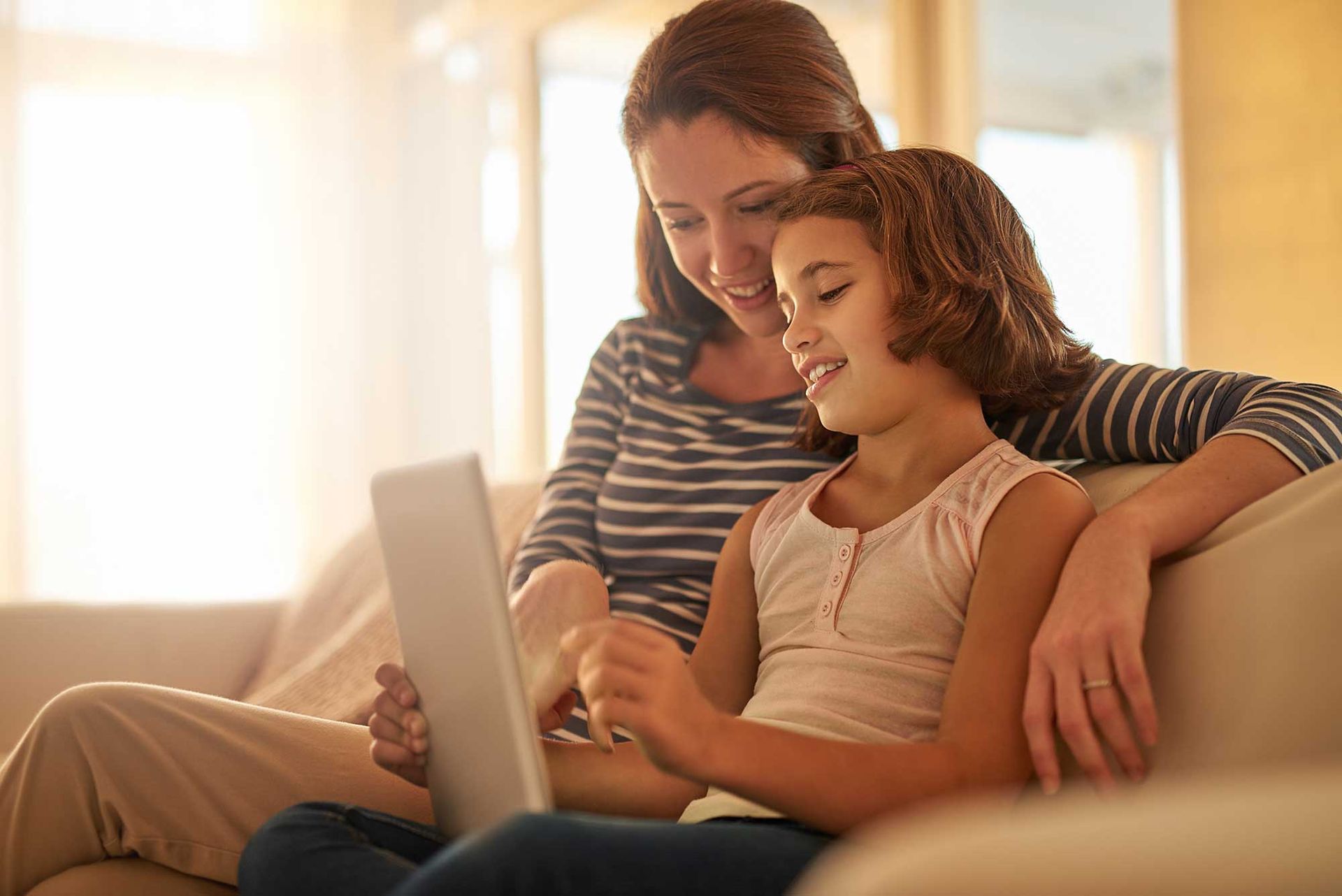 A woman and a little girl are sitting on a couch looking at a laptop.