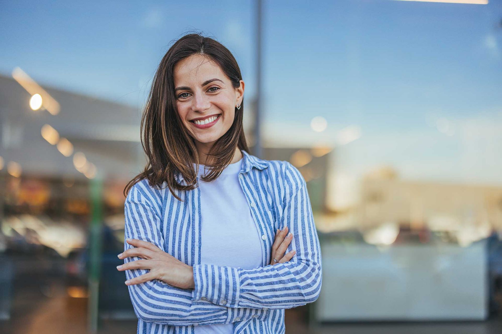 A woman in a striped shirt is standing with her arms crossed and smiling.