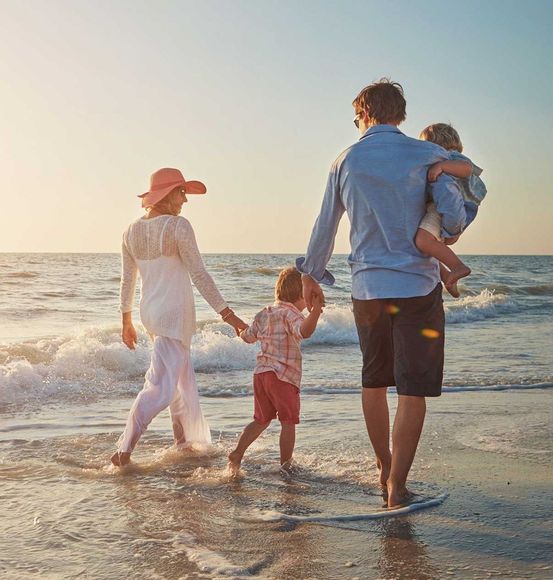 A family is walking on the beach holding hands.