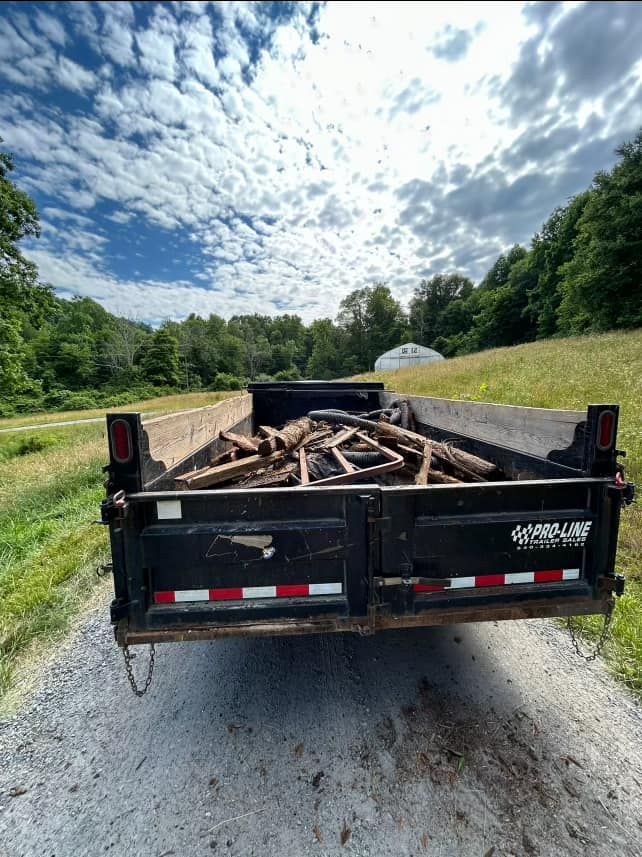 A dumpster filled with logs is parked on the side of a dirt road.