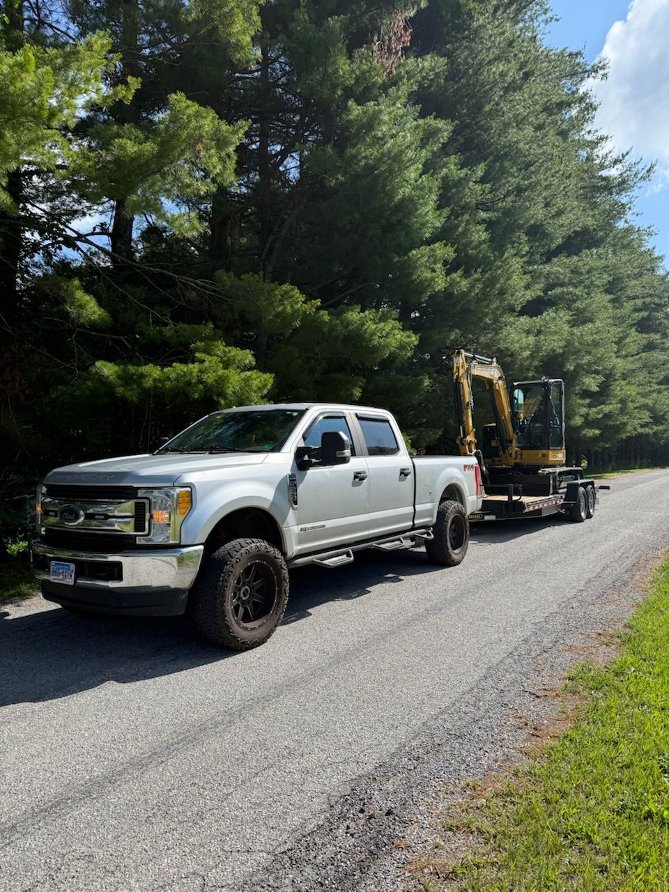 A white truck is towing a yellow excavator down a dirt road.
