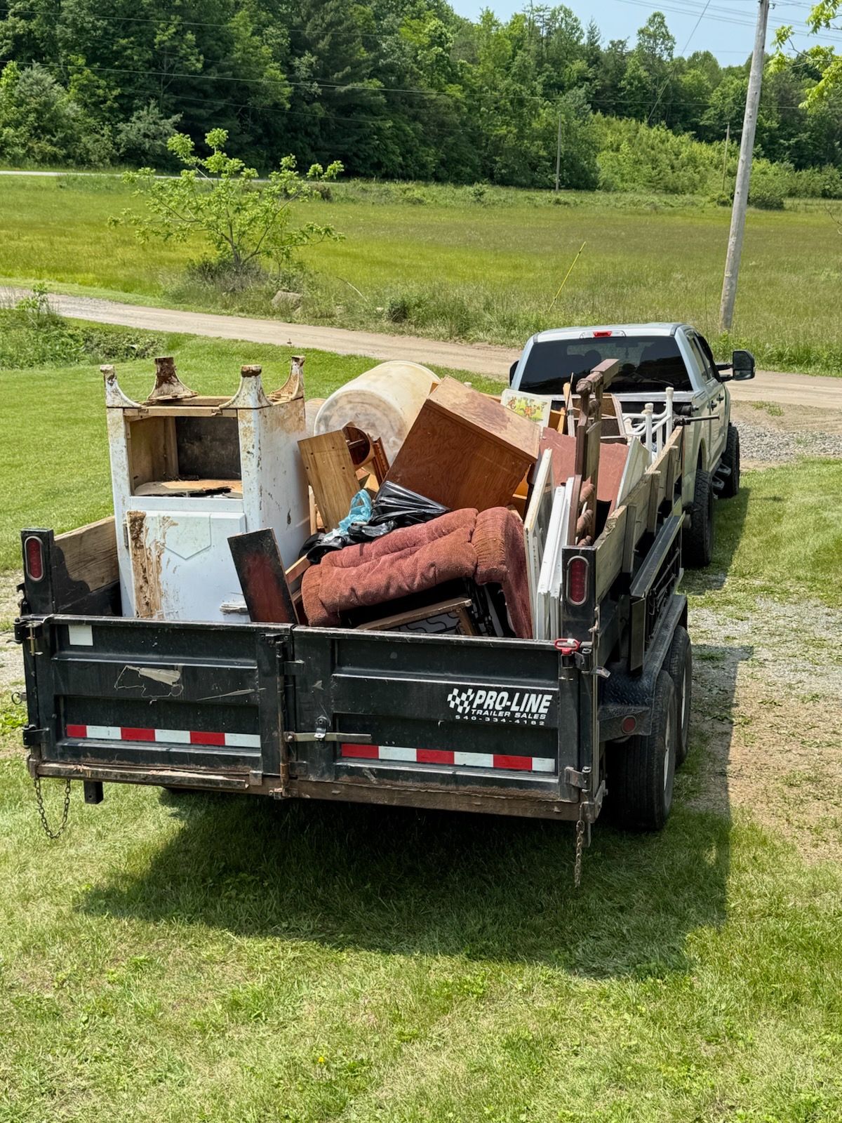 A trailer filled with furniture is parked in a grassy field next to a truck.