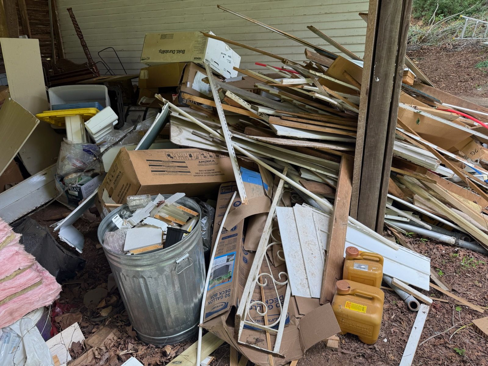 A pile of cardboard boxes is sitting next to a trash can.