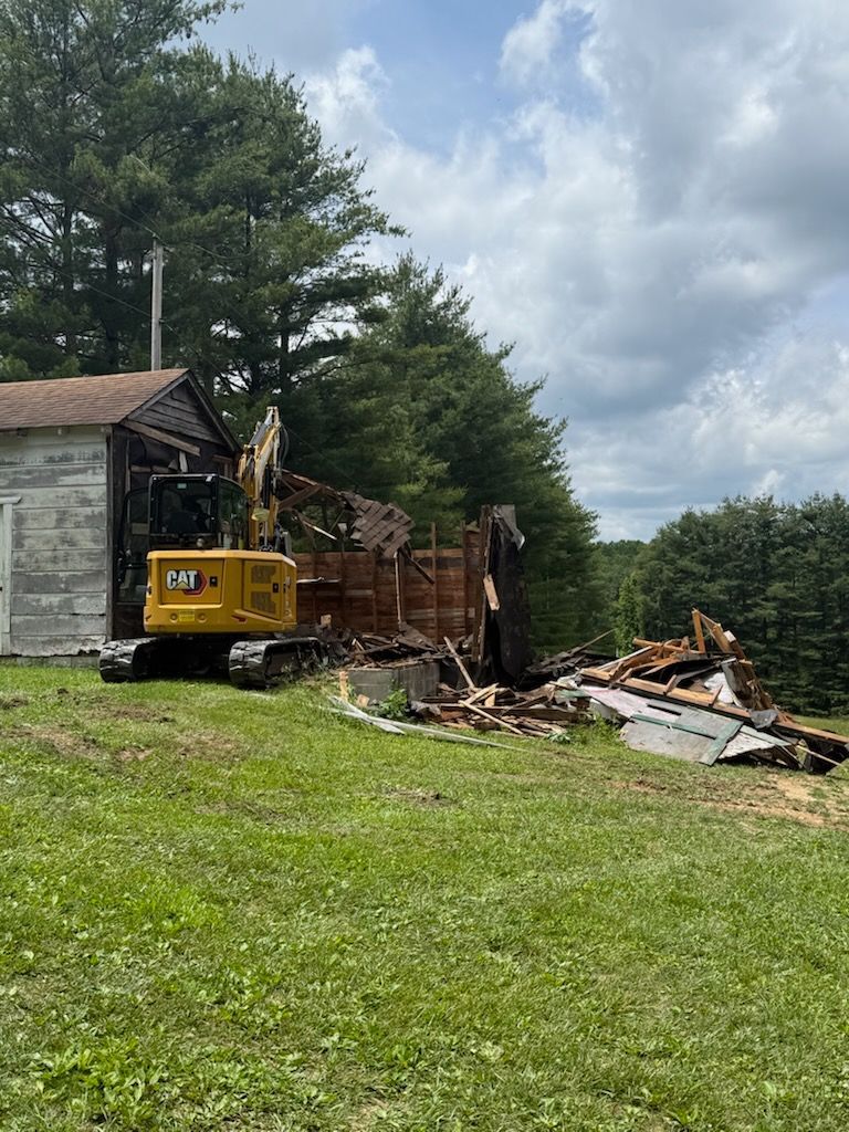 A bulldozer is demolishing a house in a grassy field.