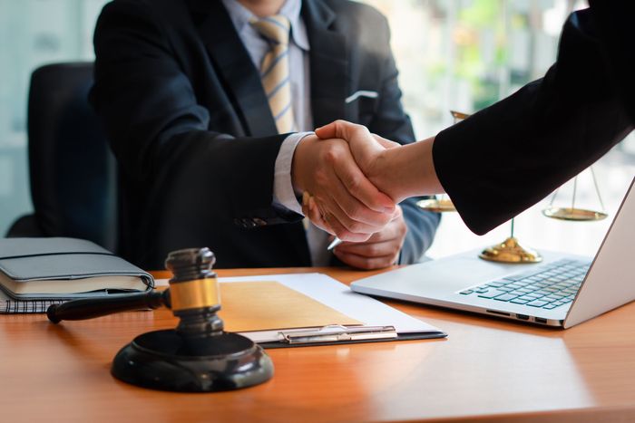 A man and a woman are shaking hands in front of a laptop.