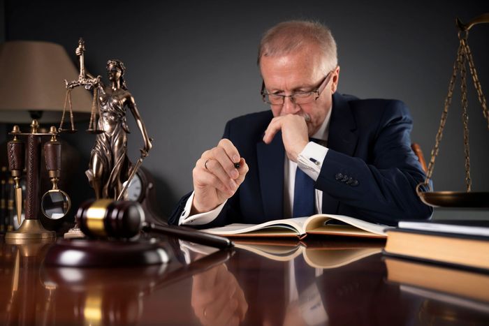 A man in a suit and tie is sitting at a desk reading a book.