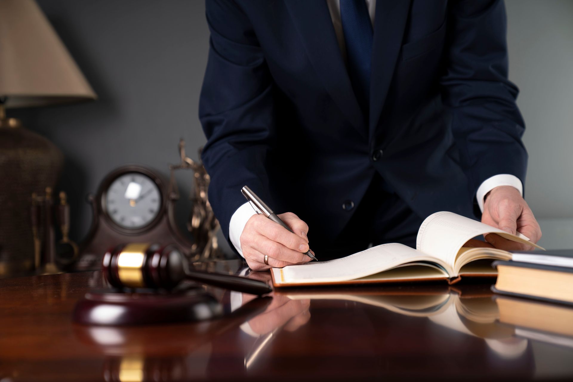 A man in a suit and tie is sitting at a desk writing in a notebook.