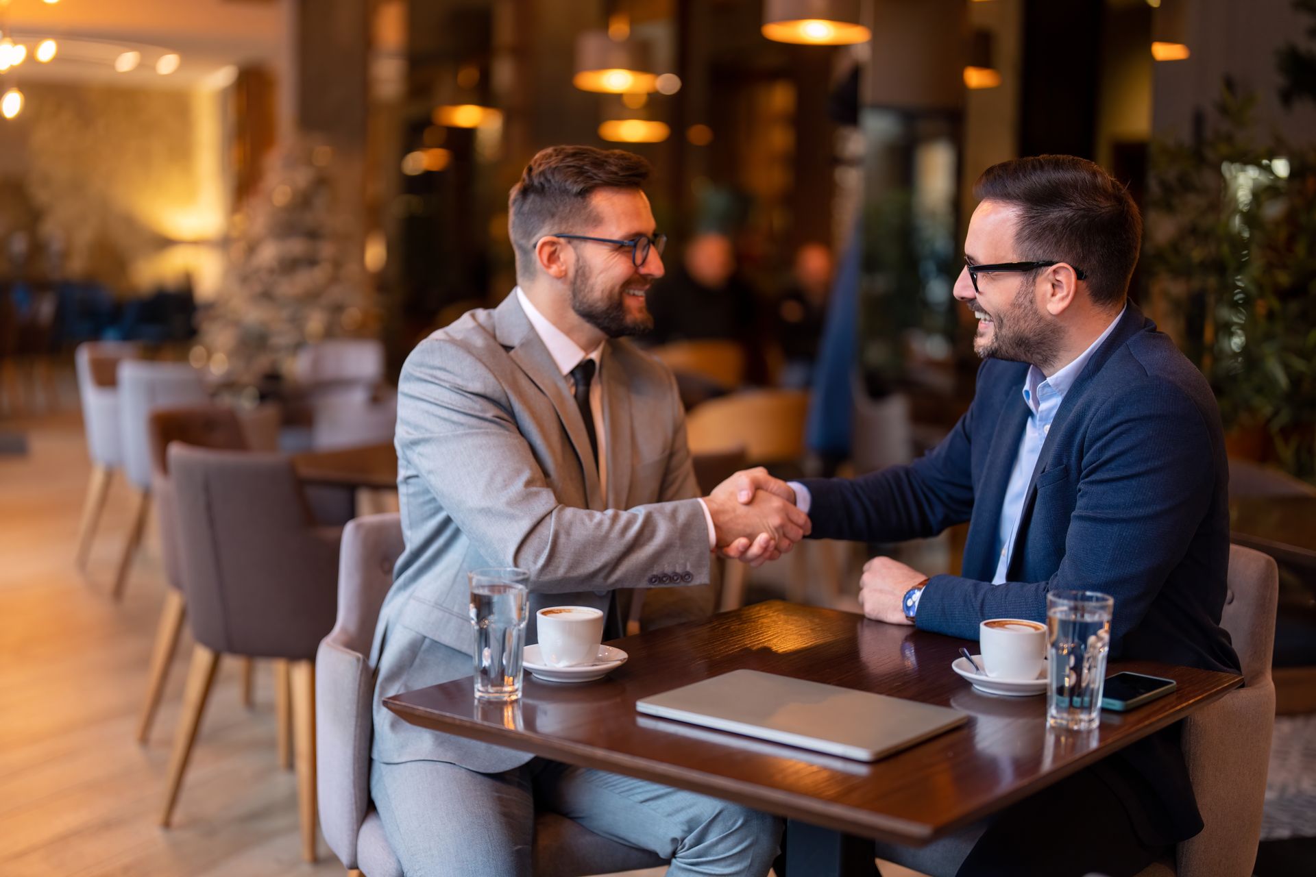 Two men are shaking hands while sitting at a table in a restaurant.