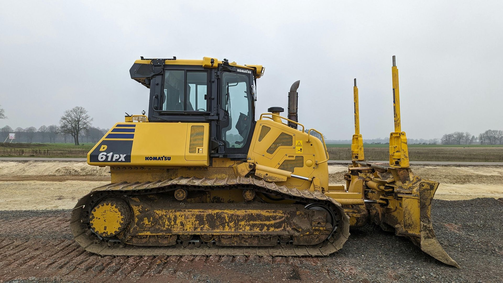 Yellow bulldozer on gravel, outdoors. The blade is down, and the tracks are visible.