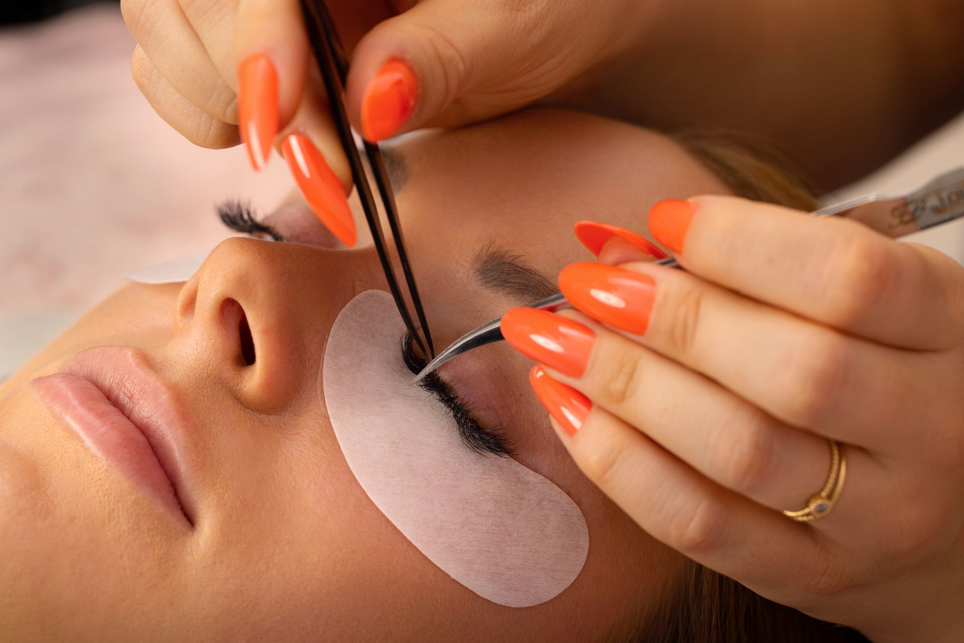 Una mujer con uñas largas de color naranja se está poniendo extensiones de pestañas.