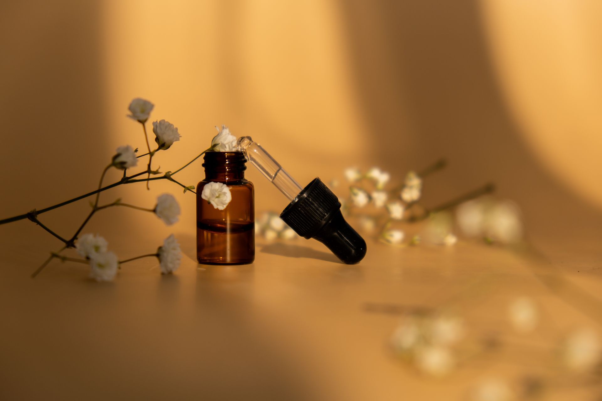 Una botella de aceite esencial con un gotero y flores sobre una mesa.